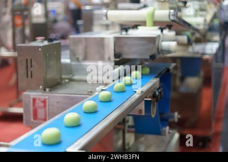 Close-up image of an automated industrial food processing system showing dough portions on a blue conveyor belt, with machinery elements in the backgr Stock Photo
