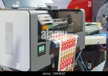 High-resolution image depicting the industrial printing process of adhesive labels, showcasing the machinery and label sheet emerging with vibrant red Stock Photo