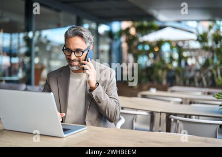 Middle aged business man talking on phone working on laptop outdoors. Copy space Stock Photo