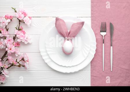 Easter lunch invitation. Festive table setting with pink spring flowers and cutlery. Bunny made of linen napkin and egg. Happy Easter holiday, menu co Stock Photo