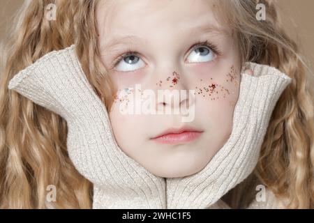 Portrait of cute little blonde girl with blue eyes and glitters on her face. Stock Photo