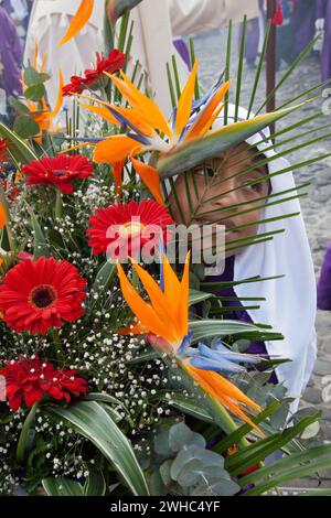 Antigua, Guatemala.  Young Cucurucho Carrying Large Vase of Flowers as he Accompanies a Procession during Holy Week, La Semana Santa Stock Photo