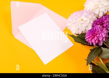 Blank greeting card mockup with pink envelope and white and purple dahlias flowers on yellow background. Blank invitation or greeting card mockup with Stock Photo