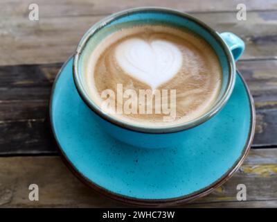 A blue ceramic cup with a heart made of milk foam on a wooden table embodies cosiness Stock Photo