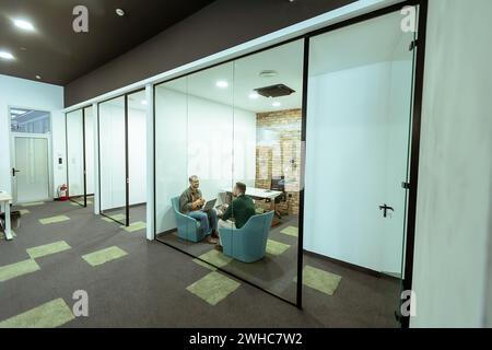 Two professionals engage in a conversation while seated comfortably in an office lounge, surrounded by greenery and contemporary design elements Stock Photo