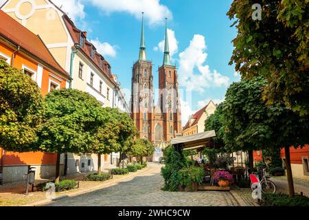 Street with cobblestone road with green trees, colorful buildings, summer cafe, Cathedral of St. John the Baptist church with two spires in old historical city centre, Ostrow Tumski, Wroclaw, Poland Stock Photo