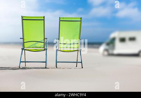 Camper on a sandy beach with blurred background, two chairs in the foreground Stock Photo