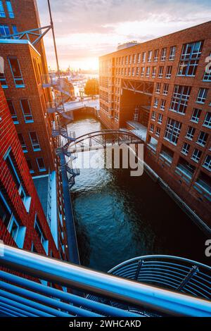 Metal staircase, bridge over canal and red brick buildings in the old warehouse district Speicherstadt in Hamburg in golden hour sunset light, Germany. View from above. Stock Photo