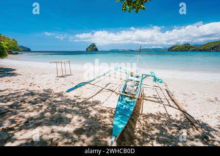 Holiday vibes. Traditional fishermen banca boat on sandy empty tropical beach. Blue ocean lagoon in background. El Nido, Philippines. Stock Photo