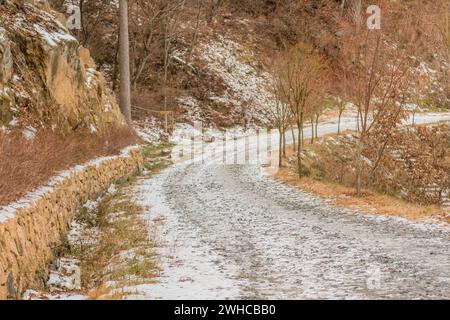 Gravel one lane road on side on mountain with snow on ground on sunny winter day Stock Photo