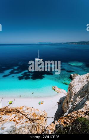 Fteri beach, island Cephalonia Kefalonia, Greece. White catamaran yacht in clear blue sea water. Tourists on sandy beach lagoon. Stock Photo