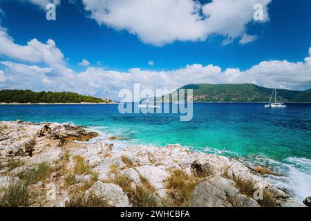 Yachts drift in middle of open crystal clear emerald green sea water near Fiskardo town. Ithaki Island in background. Amazing white cloudscape moving in blue sky, Kefalonia, Ionian islands, Greece. Stock Photo