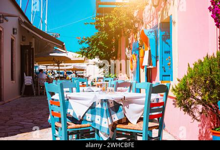 Traditional greek vivid colored tavern on the narrow Mediterranean street on hot summer day. Stock Photo