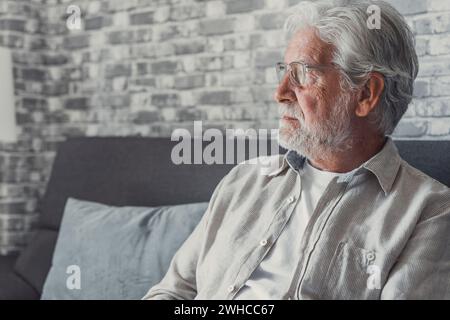 Face of senior caucasian hoary man looking away deep in sad thoughts feels lonely close up portrait, recollect memories and life moments, depressed grandfather alone indoors, yearning for wife concept Stock Photo