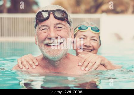 two seniors at the pool hugged together and playing - happy mature people and couple of pensioners looking at the camera smiling Stock Photo