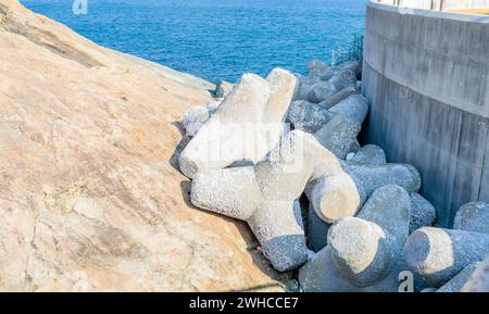 Tetrapods stacked between concrete pier and rocky shore at ocean port in South Korea Stock Photo