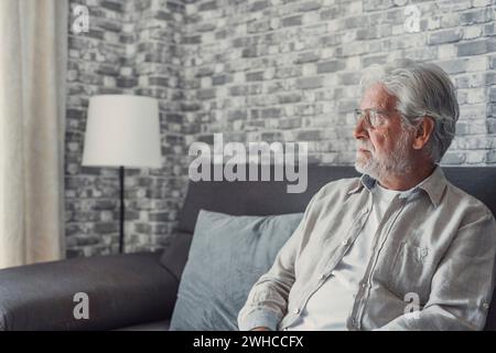 Face of senior caucasian hoary man looking away deep in sad thoughts feels lonely close up portrait, recollect memories and life moments, depressed grandfather alone indoors, yearning for wife concept Stock Photo