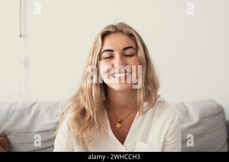 Close up overjoyed woman laughing, sitting on couch at home, head shot portrait young female chatting online with friends or relatives, looking at camera, having fun, making call or shooting video Stock Photo