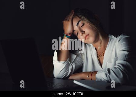 Overwhelmed young caucasian student touching head, suffering from blurry eyesight, massaging nose bridge relieving pain, feeling exhausted working late in evening on computer in office. Stock Photo
