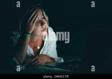 Overwhelmed young caucasian student touching head, suffering from blurry eyesight, massaging nose bridge relieving pain, feeling exhausted working late in evening on computer in bed. Stock Photo