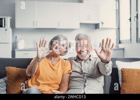 Sixty years couple, elderly parents communicates with grown up children using modern technologies makes video call, wave hands gesture of hello or goodbye sign, older generation and internet concept Stock Photo