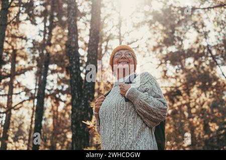 Portrait, close up of middle age caucasian woman walking and enjoying nature in the middle of trees in forest. Old mature female wearing glasses trekking and discovering. Stock Photo