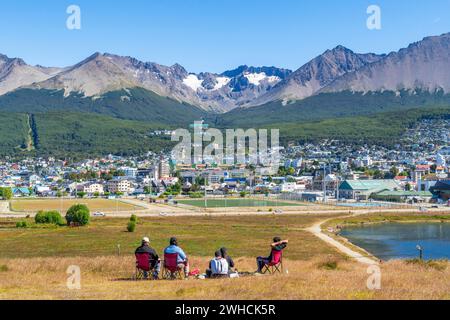 A family sits in chairs in a meadow with a view over the city of Ushuaia and the mountains Cerro Martial and Cerro del Medio, Ushuaia, Tierra del Stock Photo