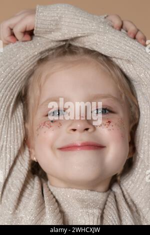 Portrait of cute little blonde girl with blue eyes and glitters on her face. Stock Photo