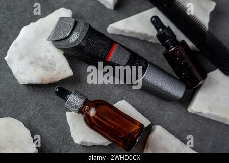 Man beard grooming items on a stone table surface, comb, oil and electric trimmer Stock Photo