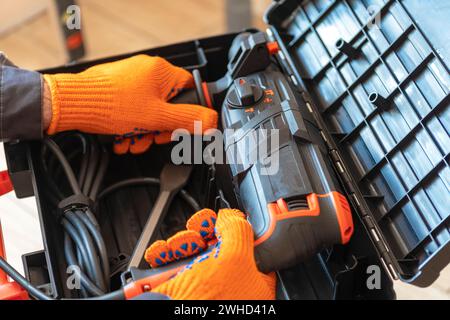 Hands with in protective gloves a rotary hammer close-up. Worker takes hammer drill perforator out of the box. Stock Photo