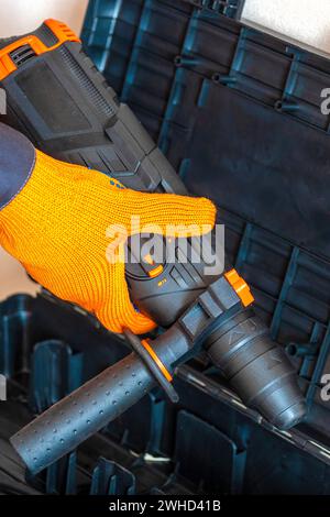 Hands in protective gloves hold  a rotary hammer. worker, professional with hammer drill perforator. Stock Photo