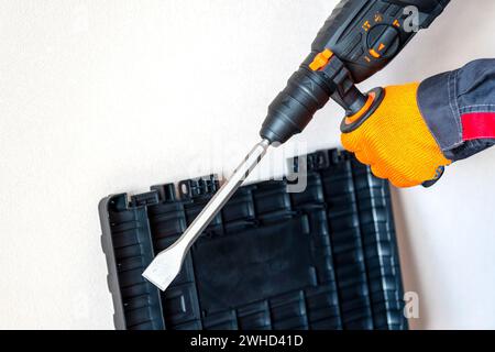 workman with a rotary hammer. Hands in protective gloves with hammer drill perforator. Copy space. Stock Photo