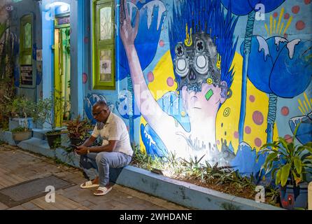Man sits on a curb in front of illuminated street art in the streets of Fort Kochi, Cochin, Kerala, India Stock Photo