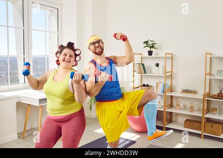 Funny overweight fat woman with bearded man in bright sportswear doing exercises at home together. Stock Photo