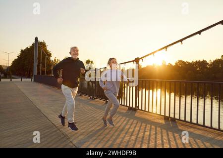 Happy healthy senior couple running along a bridge during a sports workout in the city park Stock Photo