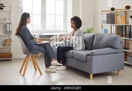 Young woman sitting at psychologist office and talking about her problems during a therapy session. Stock Photo