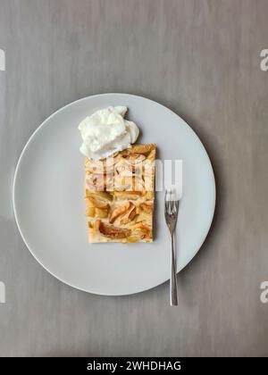 A slice of apple pie with cream served on a plate with a fork Stock Photo