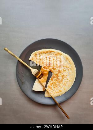 The cutlery knife and fork lie on a gray plate with a cut-off piece of pancake against a gray background Stock Photo