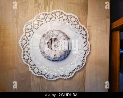 Round marble cake with powdered sugar and crumbs on a white paper tablecloth as decoration on a wooden table Stock Photo