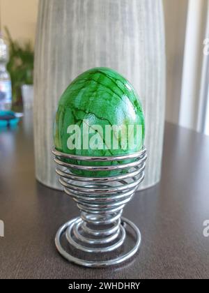 A boiled dyed green egg in a modern Easter egg cup on a wooden table Stock Photo