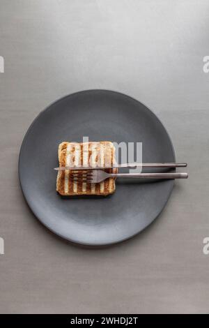 A grilled ham toast sandwich with a striped pattern lies on a plate against a gray background Stock Photo