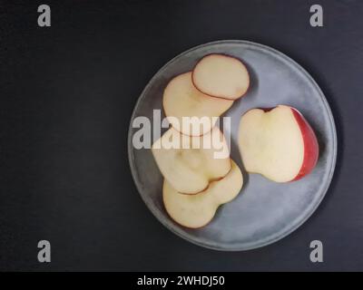 A fresh apple is sliced on a light-colored plate with a dark background Stock Photo