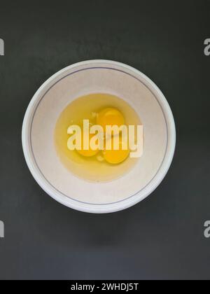 Three beaten raw eggs, egg whites and yolks in a white bowl Stock Photo