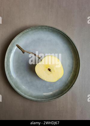 A fresh halved apple with core lies on a pastel-colored plate and light grey background Stock Photo