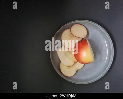 A fresh apple is sliced on a light-colored plate with a dark background Stock Photo