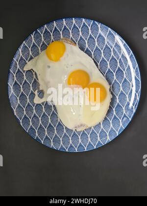 three fried eggs on a blue and white plate Stock Photo