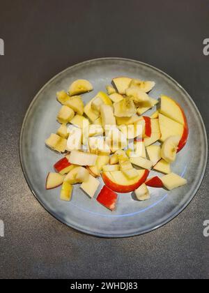 Pieces of apple with red apple skin cut into small pieces as a fruit salad on a light blue plate Stock Photo