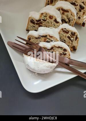 Close-up of several slices of Christmas stollen on a white porcelain plate with knife and fork Stock Photo