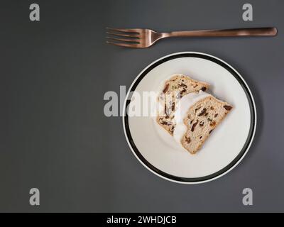 Two slices of Christmas cake with white powdered sugar on a white plate with a black rim and a copper-colored fork Stock Photo