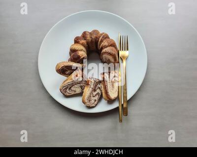 Pieces of cut marble cake lie on the light gray plate next to the golden cutlery Stock Photo